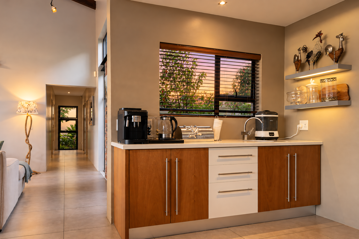 A modern kitchen area featuring wood-toned cabinetry, white drawers, a sink, and illuminated floating shelves, seamlessly integrated into an open-plan living space.