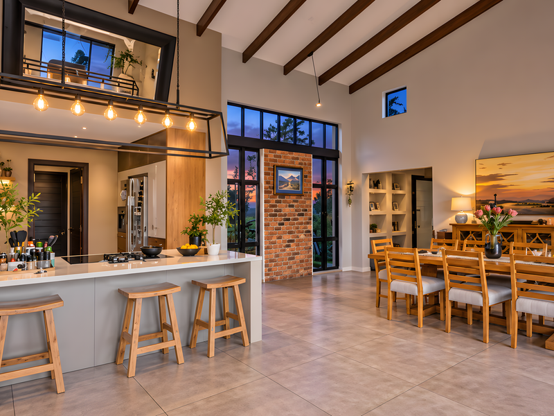 Spacious open-plan living and kitchen area featuring exposed timber beams, a modern kitchen island, and a striking exposed brick feature wall with large windows.
