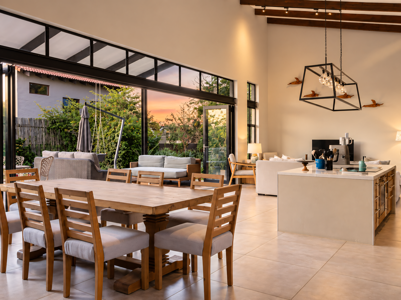 Spacious open-plan living and dining area featuring high ceilings with exposed timber beams, large format floor tiles, and seamless indoor-outdoor flow via bi-fold doors.