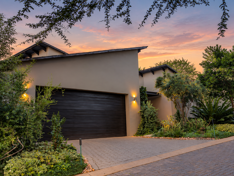 Modern front facade featuring a sleek double garage door, paved driveway, and well-maintained landscaped garden under a sunset sky.