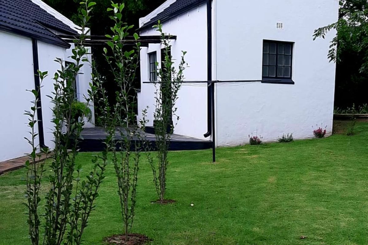 A view of the rear exterior of the guest house, featuring white painted walls, dark roof tiles, and a well-maintained lawn with a timber deck.