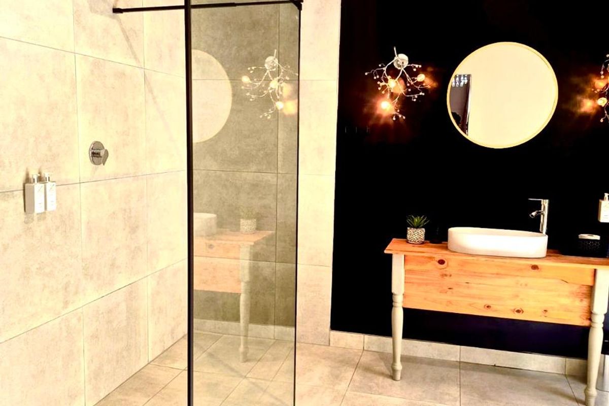 Modern bathroom featuring a spacious walk-in shower with a glass screen, rain shower head, and a stylish vessel sink vanity against a dark accent wall.