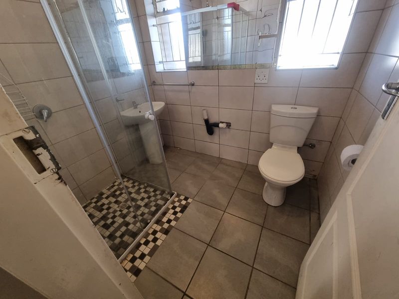 A functional bathroom featuring a shower enclosure, pedestal basin, and toilet, with neutral wall and floor tiling throughout.