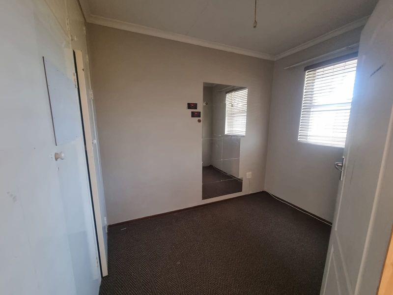 An empty bedroom featuring carpeted flooring, a built-in wall mirror, and venetian blinds, presenting a blank canvas for potential renovation or restyling.