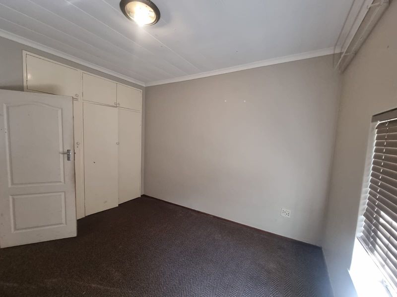 An empty bedroom featuring built-in cupboards, carpeted flooring, and venetian blinds, offering a neutral canvas for personalization.