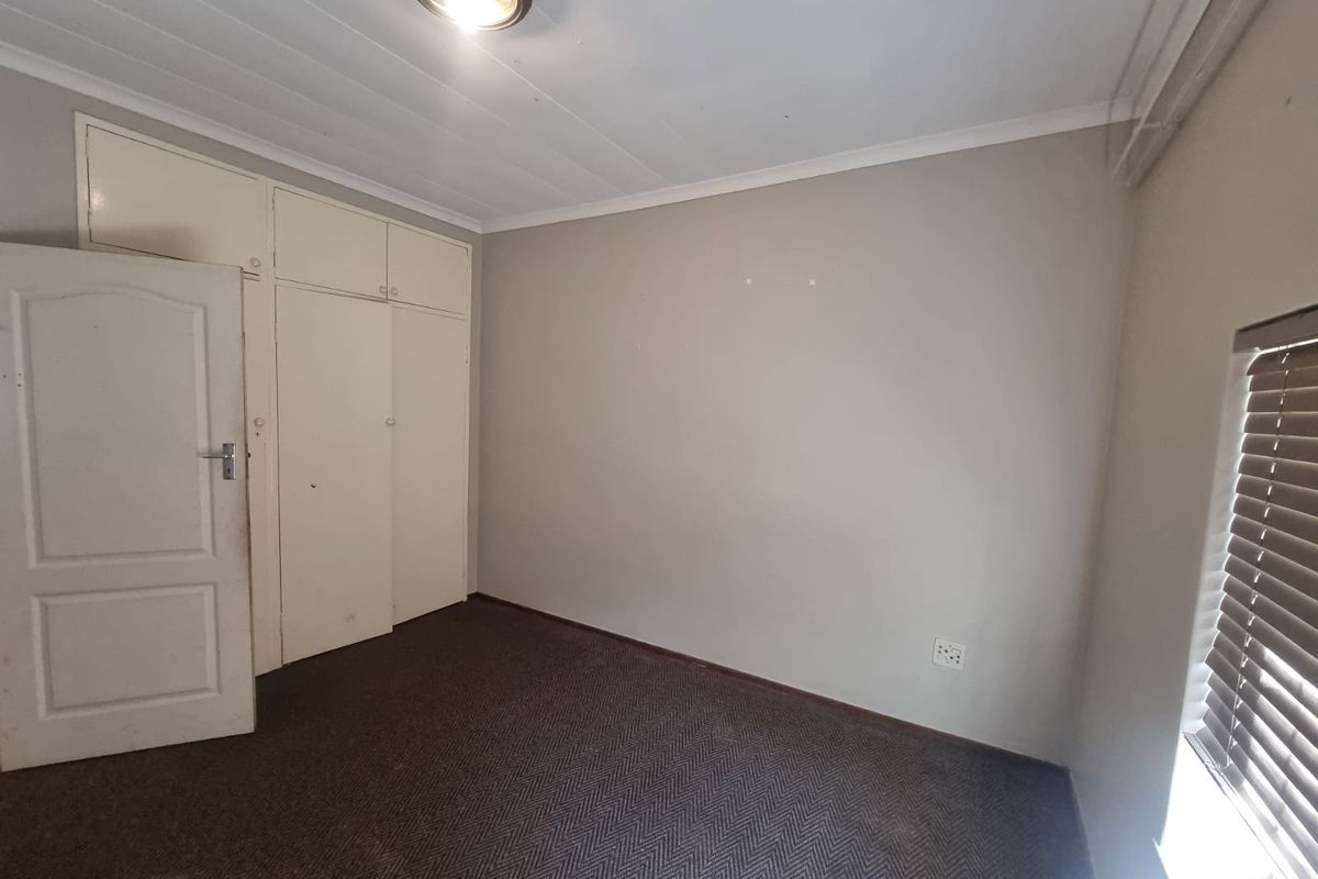 An empty bedroom featuring built-in cupboards, carpeted flooring, and venetian blinds, offering a neutral canvas for personalization.