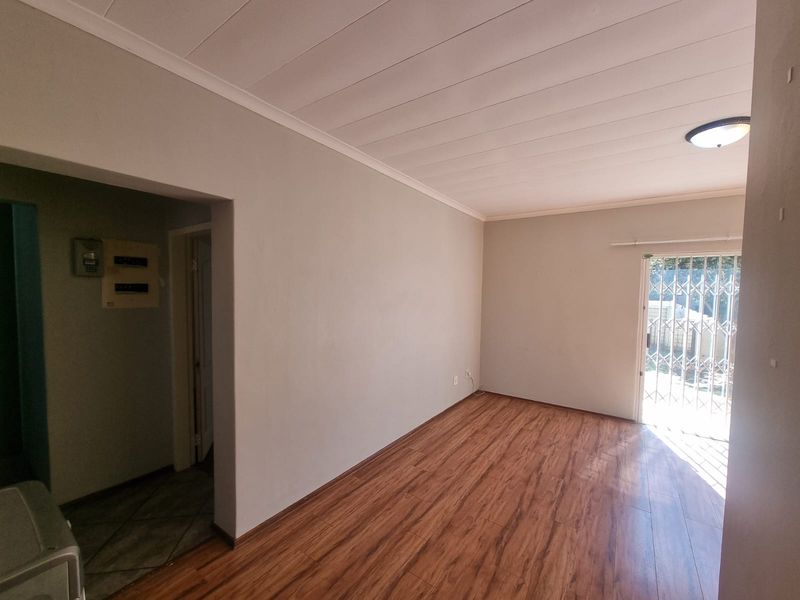 An empty living room featuring laminate flooring, a security gate leading to the exterior, and a neutral wall finish.