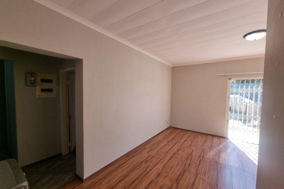 An empty living room featuring laminate flooring, a security gate leading to the exterior, and a neutral wall finish.