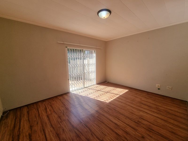 An empty living room featuring laminate flooring, a ceiling light fixture, and a sliding door with a security gate leading outside.