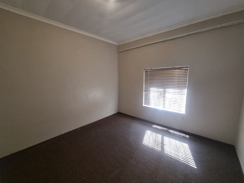 An empty bedroom featuring carpeted flooring, a coved ceiling, and a window fitted with venetian blinds.