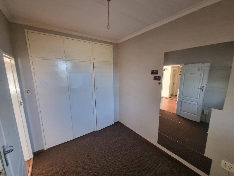 A vacant bedroom featuring built-in cupboards, a large wall-mounted mirror, and carpeted flooring, offering a blank canvas for renovation.