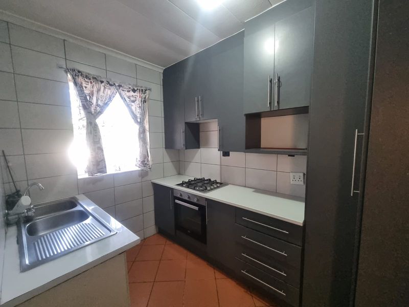 A functional kitchen featuring modern dark grey cabinetry, a gas hob, built-in oven, double sink, and tiled finishes throughout.