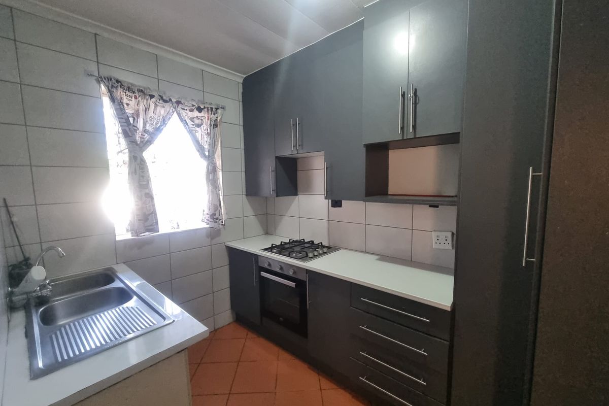 A functional kitchen featuring modern dark grey cabinetry, a gas hob, built-in oven, double sink, and tiled finishes throughout.