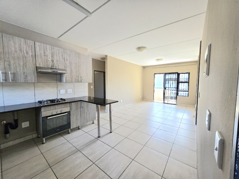 Open-plan kitchen and living area featuring tiled floors, modern wood-look cabinetry, built-in oven and hob, and access to a balcony through a security gate.
