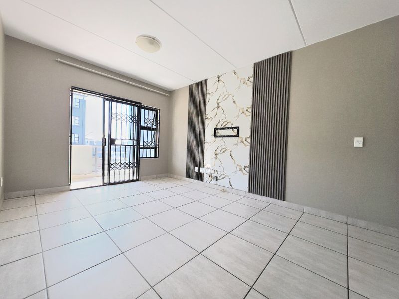 A bright, empty living room featuring large floor tiles, a decorative marble-look feature wall with timber slats, and access to a balcony via sliding doors.