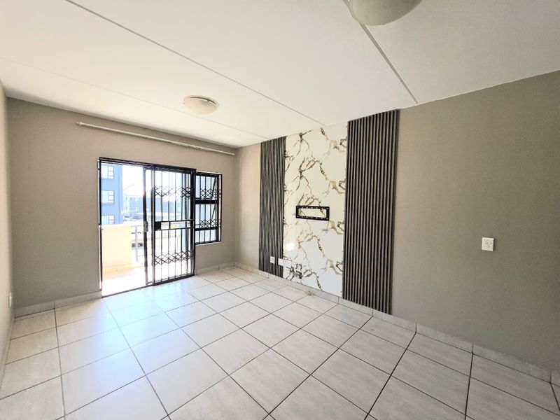 A bright, empty living room featuring modern marble-effect and slatted wall paneling, tiled flooring, and direct access to a balcony through a sliding door.
