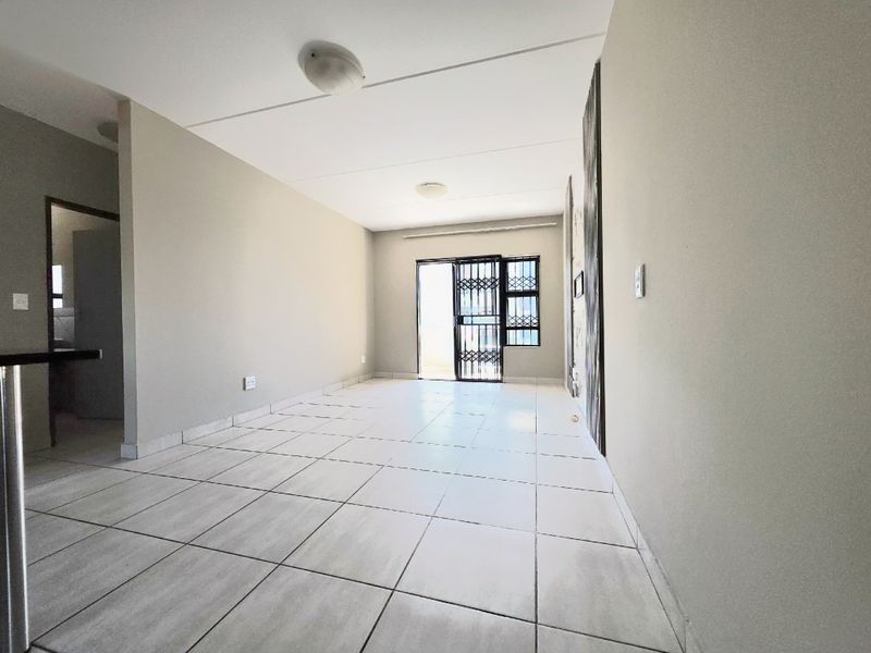 A bright, empty living area featuring neutral tiled flooring and a security gate leading to an outdoor space.