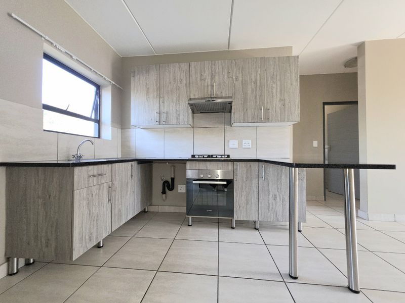 Modern kitchen featuring light wood-grain cabinetry, granite countertops, built-in oven with gas hob, and tiled flooring in an open-plan layout.