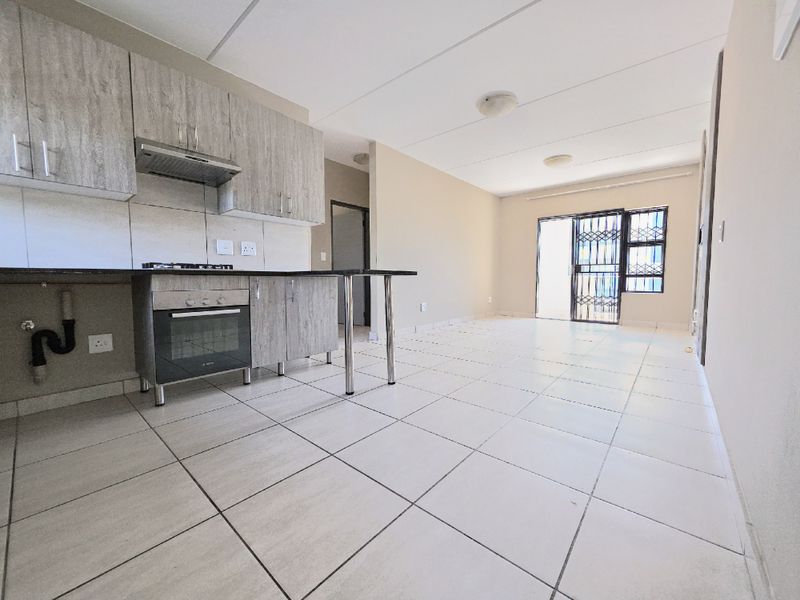 Open-plan living area featuring a modern kitchen with built-in cabinetry, oven, and hob, leading to a bright space with tiled flooring and sliding door access.