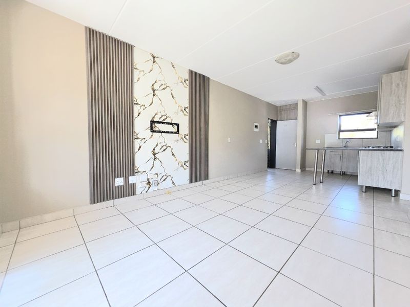 Spacious open-plan living and kitchen area featuring modern tiled flooring, a decorative feature wall, and functional built-in kitchen cabinetry.