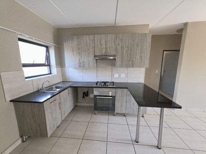 Modern kitchen featuring wood-look cabinetry, granite countertops, a gas hob, built-in oven, and a breakfast bar, offering a functional and clean workspace.