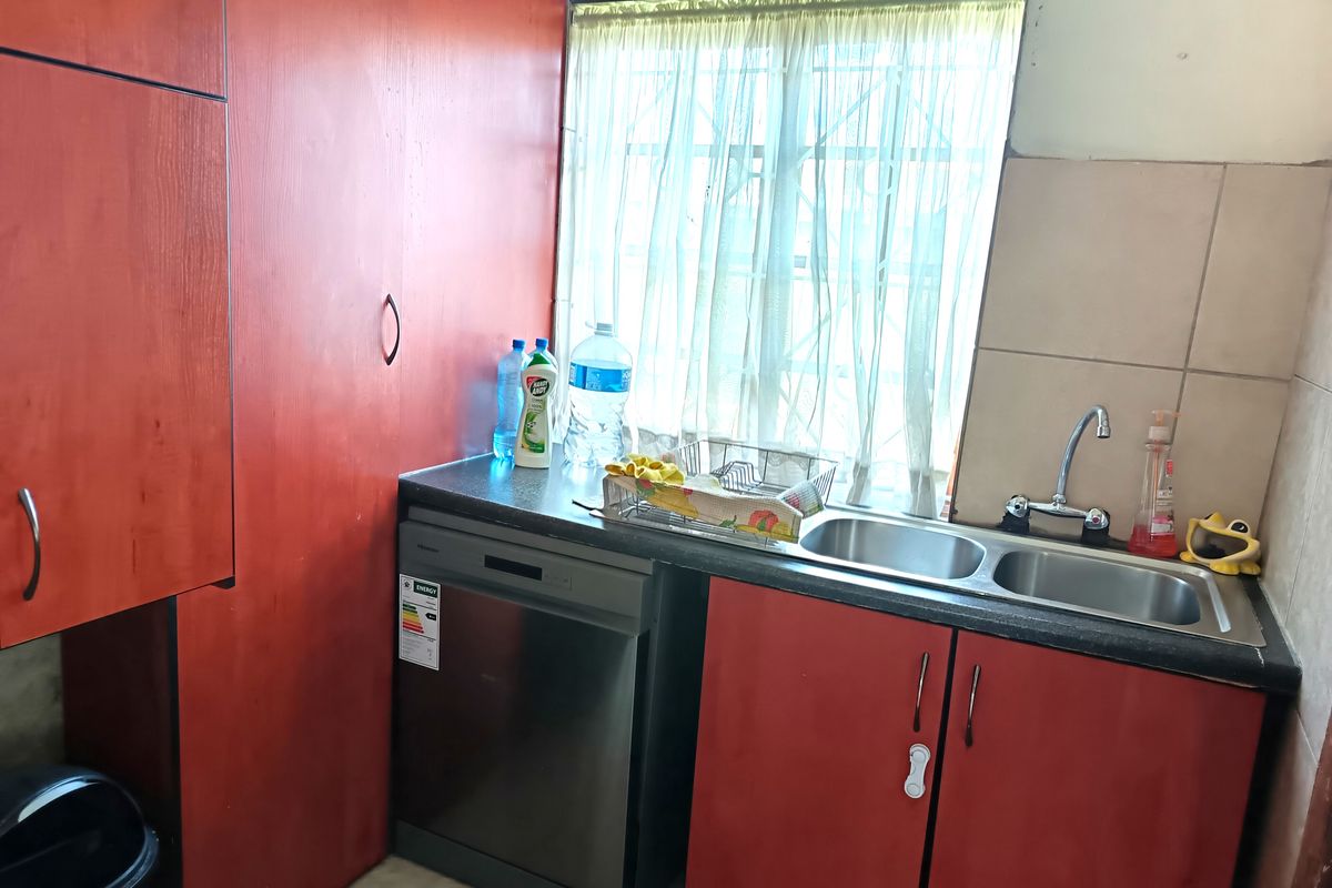 A functional kitchen area featuring red cabinetry, a double stainless steel sink, and a built-in dishwasher space with a window for natural light.