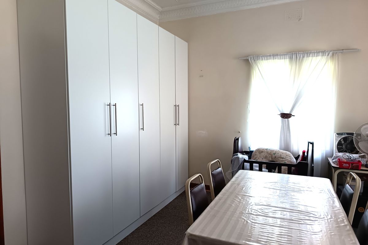 A bedroom featuring a large, modern floor-to-ceiling built-in wardrobe with white cabinetry and decorative ceiling cornicing.
