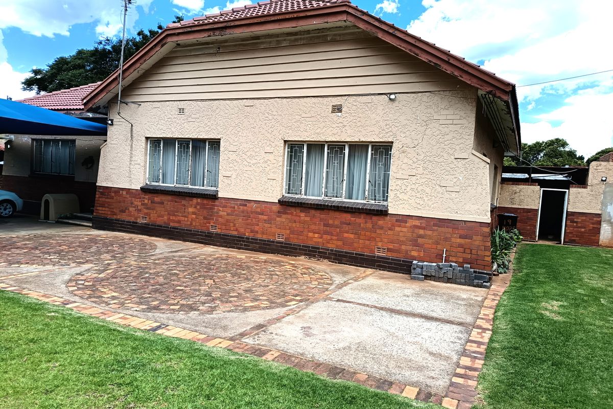 Rear view of a single-story house featuring a brick and plaster facade, tiled roof, and a paved patio area leading to a lawn.