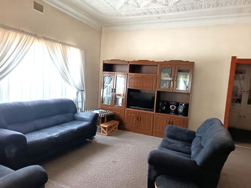 A spacious living room featuring high ceilings with decorative cornicing and a large window allowing for natural light.