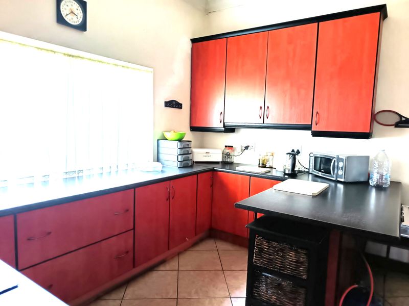 A functional kitchen featuring red cabinetry with black trim, dark countertops, and tiled flooring, offering ample storage and workspace.