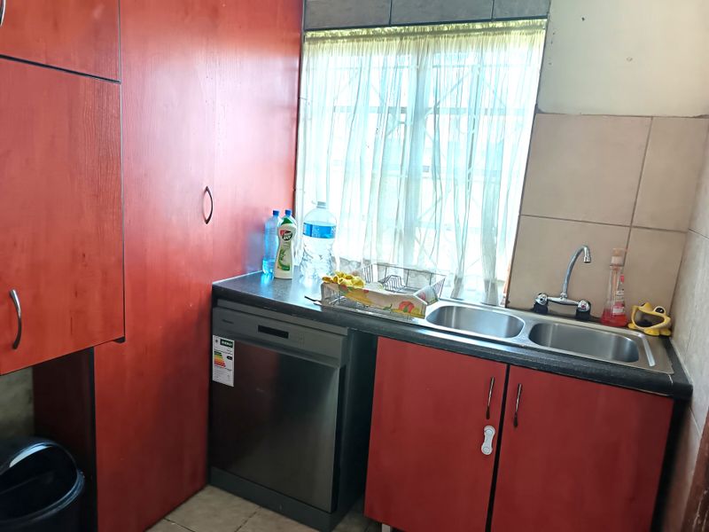 A functional kitchen area featuring red cabinetry, a double stainless steel sink, and a built-in dishwasher space with a window for natural light.