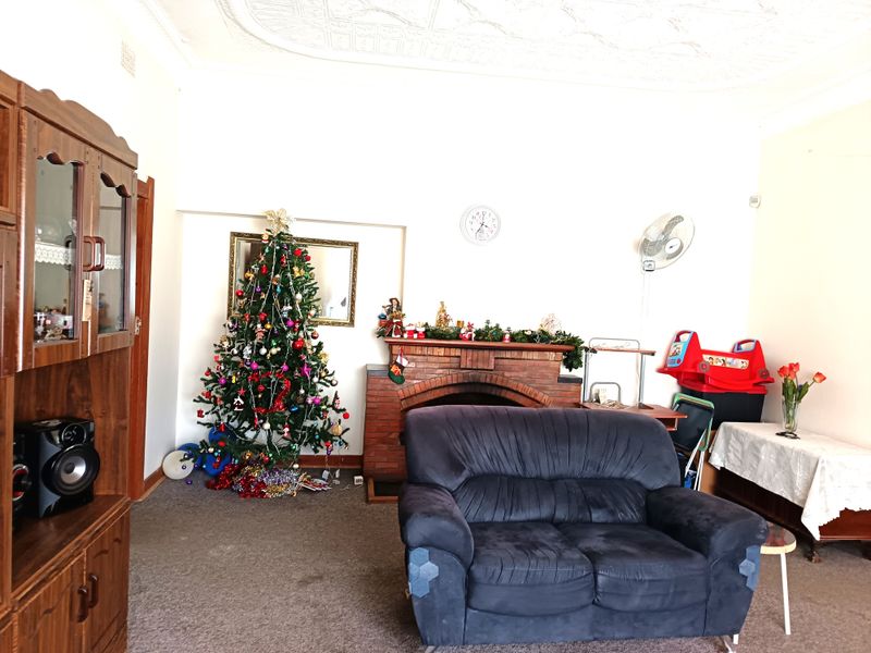 A living room featuring a traditional brick fireplace, decorative ceiling molding, and carpeted flooring, offering a classic layout with potential for modernization.