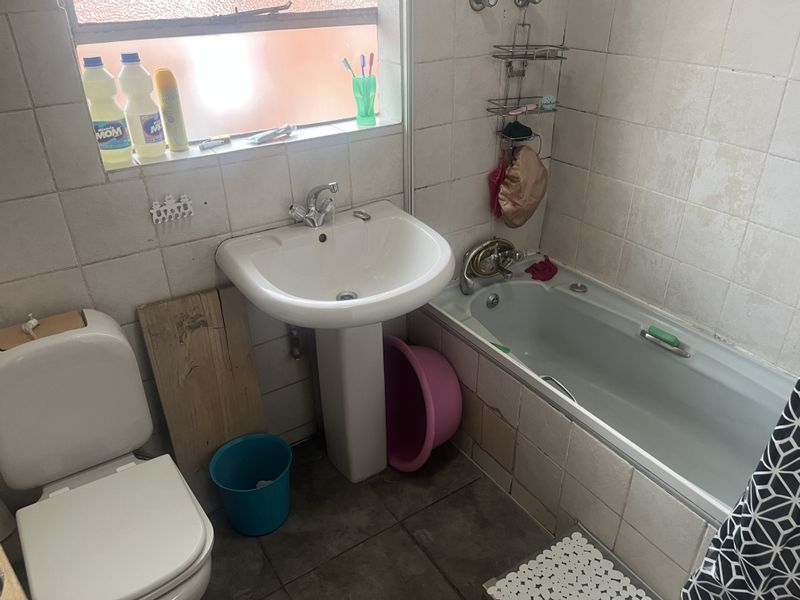 A functional bathroom featuring a pedestal basin, bathtub, and toilet with tiled finishes, requiring cosmetic updates to improve its overall condition.