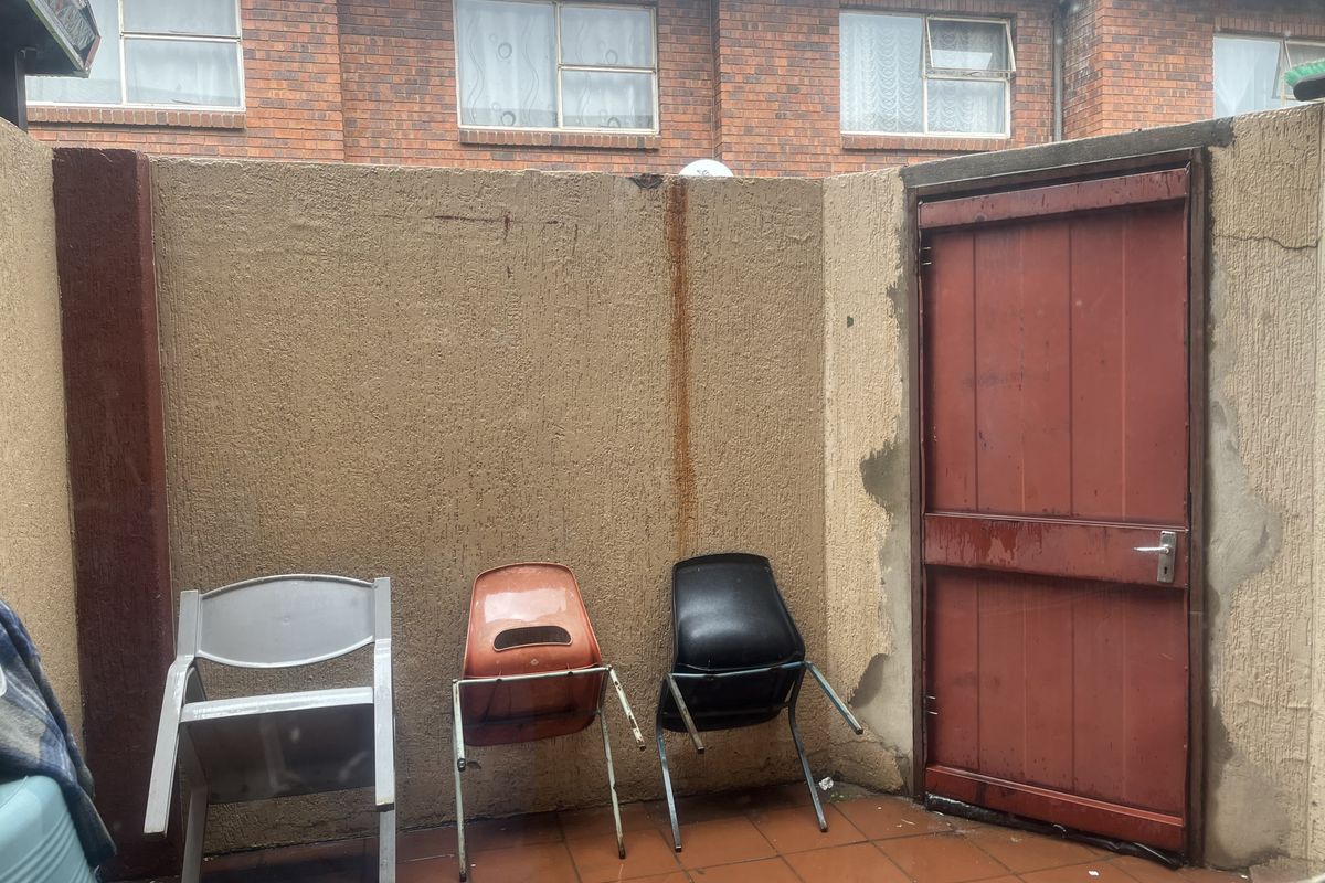 A small rear courtyard area featuring tiled flooring, a solid door, and a boundary wall showing signs of weathering and staining.