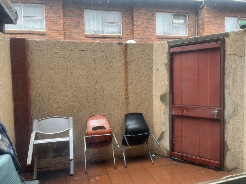 A small rear courtyard area featuring tiled flooring, a solid door, and a boundary wall showing signs of weathering and staining.