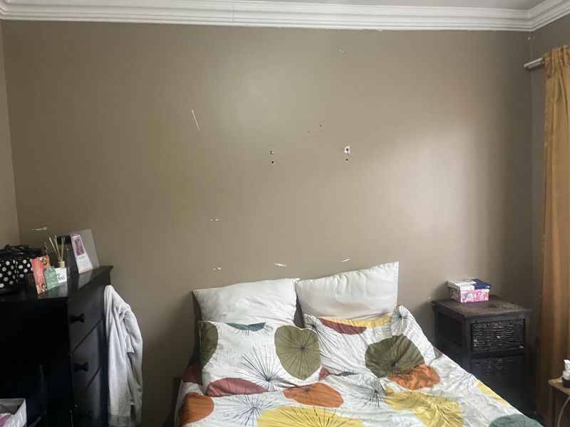 A bedroom featuring crown molding and a curtain rail, currently showing visible wall surface damage and scuffs requiring cosmetic repair.