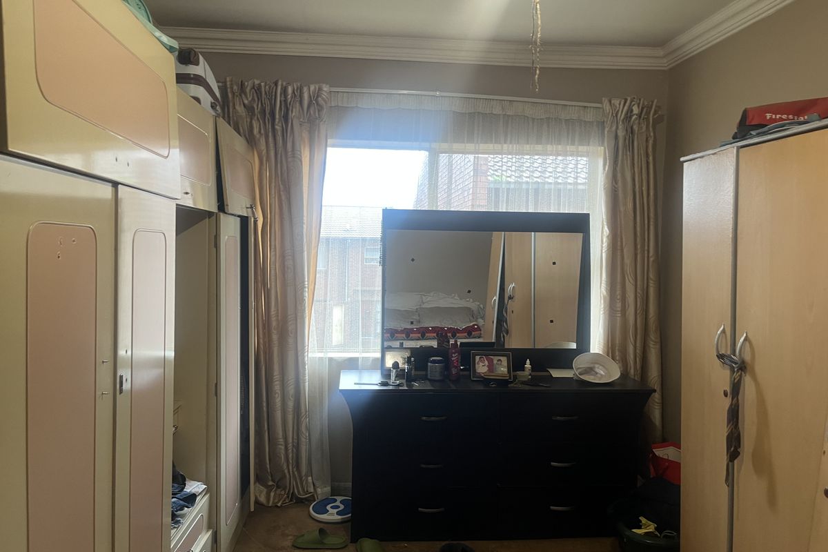 A bedroom featuring built-in cupboards and a window with natural light. The room requires cosmetic updates to the flooring and cabinetry.