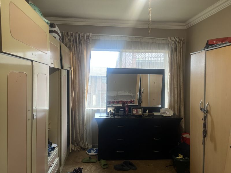 A bedroom featuring built-in cupboards and a window with natural light. The room requires cosmetic updates to the flooring and cabinetry.