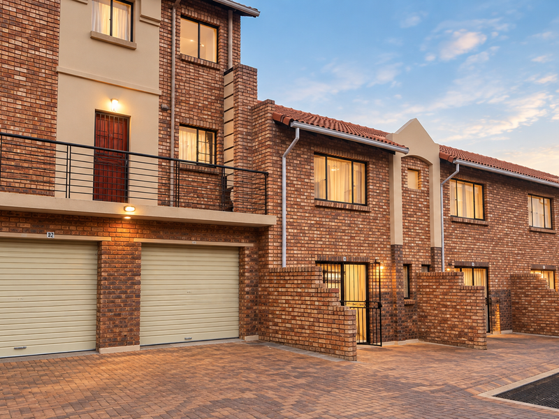 A well-maintained townhouse exterior featuring a brick facade, double garage with roller doors, and a private balcony with metal railings.