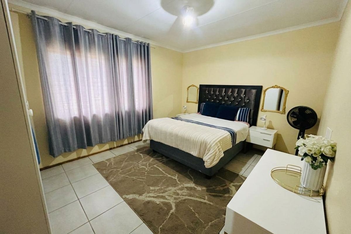 A functional bedroom featuring tiled flooring, neutral wall finishes, and large windows with curtain tracks, providing a comfortable and well-lit sleeping space.