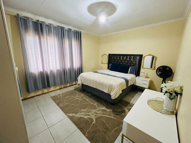 A functional bedroom featuring tiled flooring, neutral wall finishes, and large windows with curtain tracks, providing a comfortable and well-lit sleeping space.