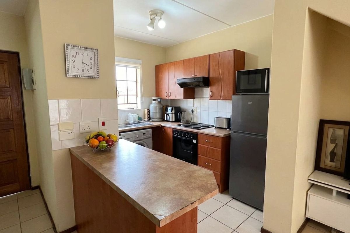 Compact kitchen featuring wooden cabinetry, laminate countertops, built-in oven with hob, extractor fan, and tiled flooring, offering a functional layout for daily use.