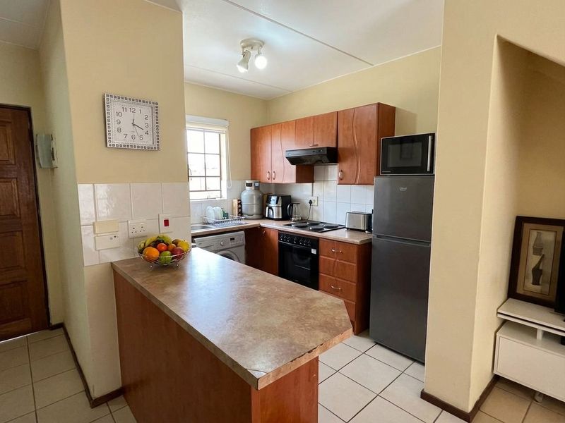 Compact kitchen featuring wooden cabinetry, laminate countertops, built-in oven with hob, extractor fan, and tiled flooring, offering a functional layout for daily use.
