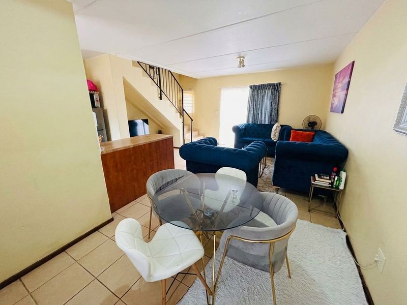 Open-plan living and dining area featuring tiled flooring, a breakfast counter, and a staircase leading to the upper level.