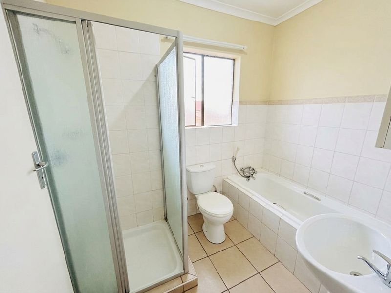 A functional bathroom featuring a separate shower enclosure, bathtub, toilet, and pedestal basin with neutral wall and floor tiling.