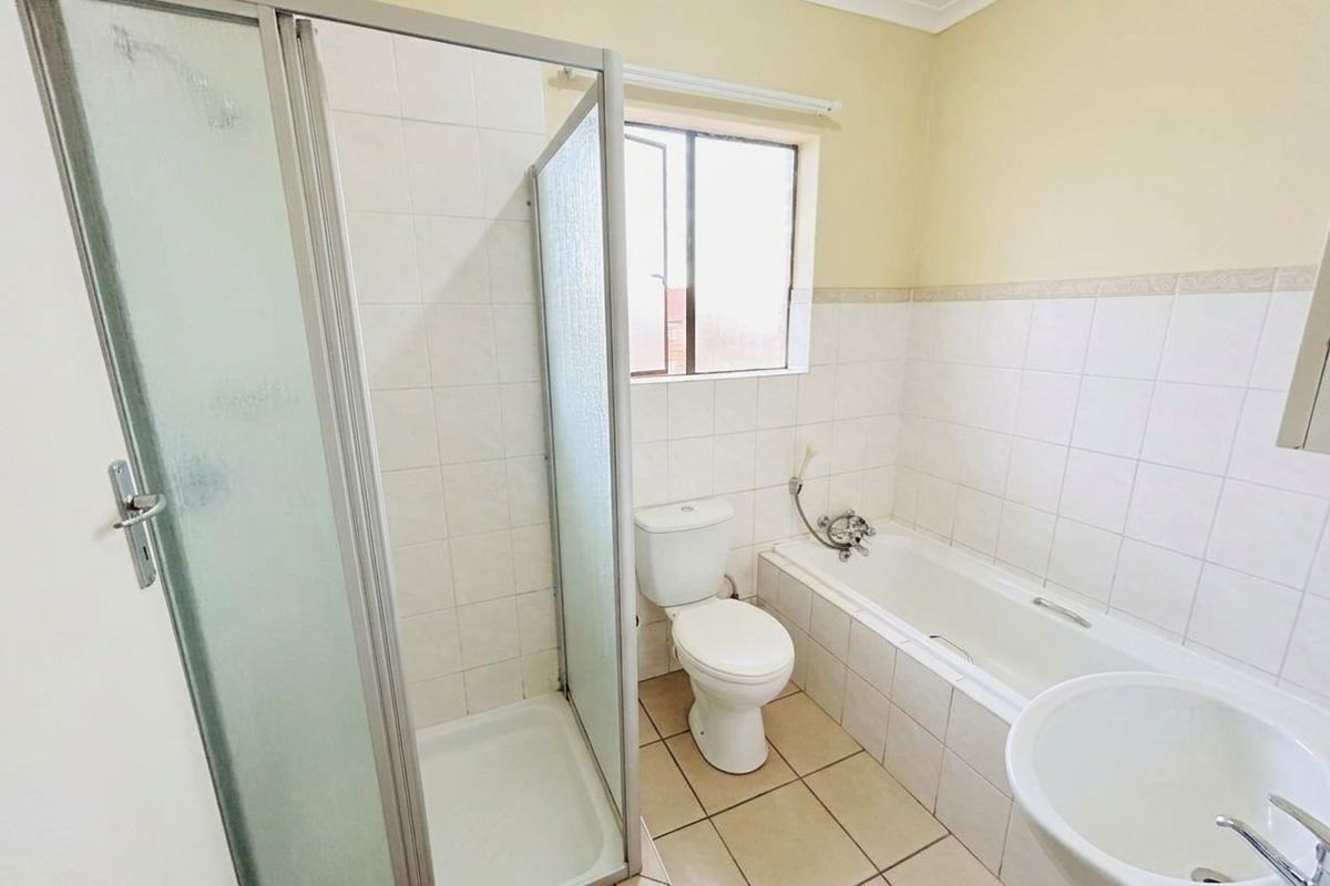 A functional bathroom featuring a separate shower enclosure, bathtub, toilet, and pedestal basin with neutral wall and floor tiling.