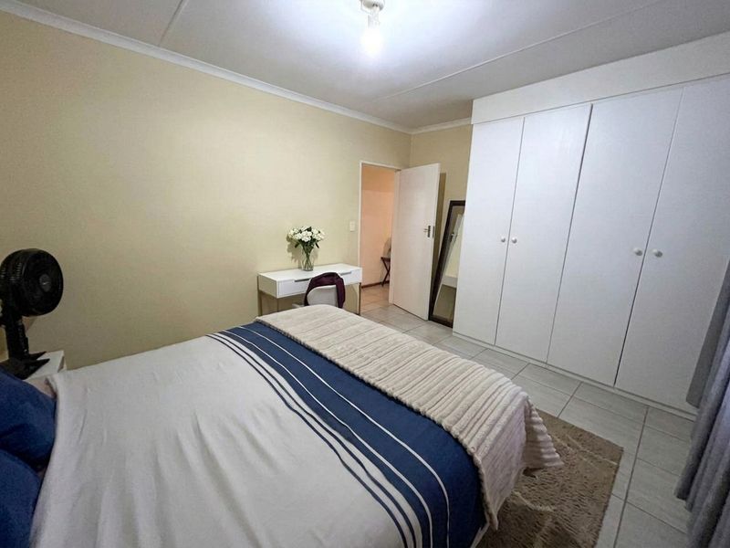 A functional bedroom featuring built-in cupboards, neutral wall finishes, and tiled flooring, providing a clean and practical living space.