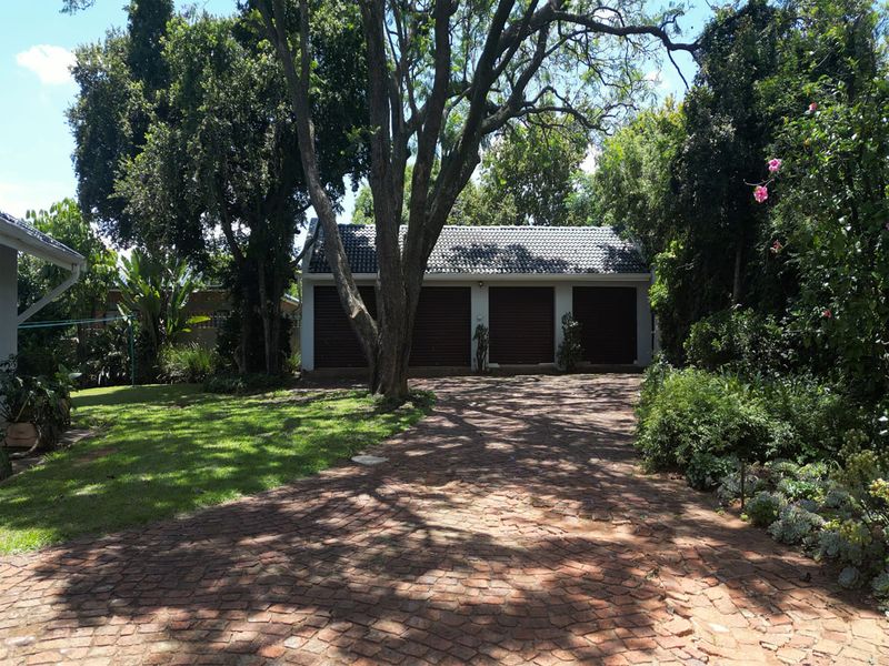 A detached triple garage building featuring dark roller doors, set within a mature garden with a paved driveway and established trees.