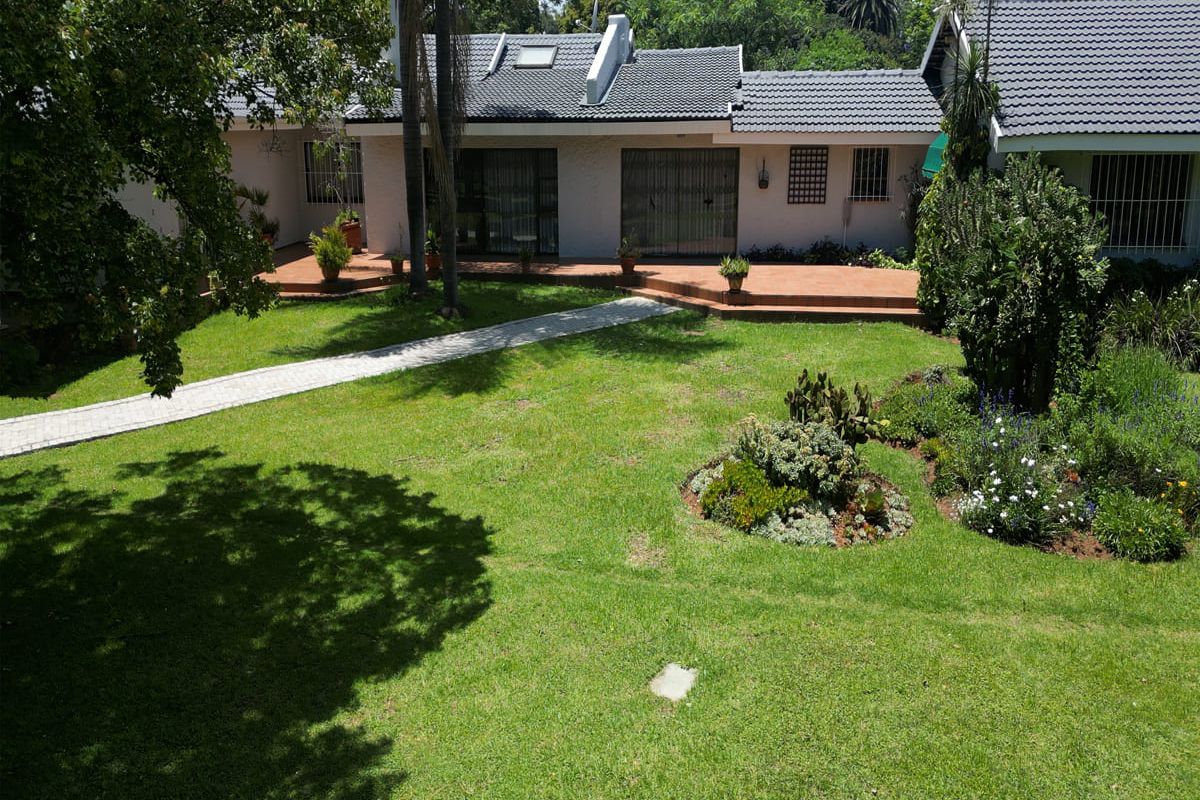 A view of the rear garden featuring a paved walkway, landscaped beds, and a covered patio area attached to the main house structure.