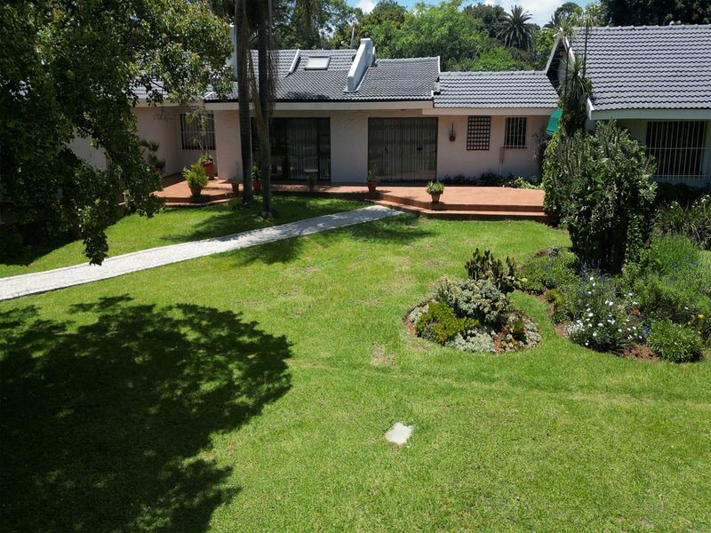 A view of the rear garden featuring a paved walkway, landscaped beds, and a covered patio area attached to the main house structure.